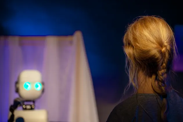 Young girl seen from behind looking at a robot. Photo.